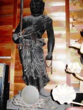 年季の入った赤い色の木壁に装飾品に囲まれて展示されている黒い木造不動明王立像の写真