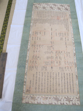 細かい文字がたくさん書かれている緑色の掛け軸がやや斜めに傾いている写真