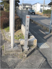 歩道のすぐ横に「十五条」と書かれた小さい石碑がありその横に石の台の上に設置された鉄筋の棒が手前と奥に2本設置されている写真