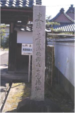 瓦屋根の門の近くに文字の書かれた大きな石柱が立っている写真