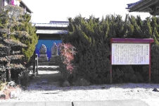 砂利の地面に赤紫色の枠の説明版が設置されその左側に造られた木々に囲まれた細い砂利道の奥に句碑が並んでいる様子の写真