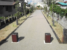 茶色の低い柱が2つ設置されたコンクリート造りの一本道の写真