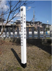 北方町朝日神社朝日神社のクロガネモチと書かれた白い標柱が青空の下太陽の光を受けて影をのばしている写真