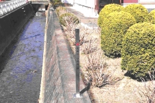 用水路の上の生垣に設置された灰色の標柱の写真