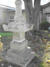 家が奥にある木の立っている土地に白い修復された石塔が立っている写真