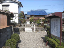 小さな白い2段の階段の手前に石柱と奥に建っている小さな社を正面から説明版を遠くから撮影した写真