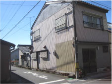 青空の下家の周囲を鉢植えで囲んでいる一般家屋を斜めから写した写真