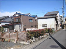 青空の下垣根に囲まれた一般家屋の庭を斜めから撮影した写真