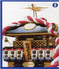 屋根の上に鶴が立ち、赤と白のしめ縄で飾られた漆塗りの神輿を撮影した写真