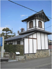 白い壁に瓦屋根の2階建ての小屋のような建物を道路の向かい側から撮影した写真