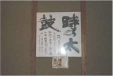 「時の太鼓」と書かれた色紙が壁の木枠にはめられて飾られている写真