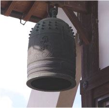 晴れた日に寺の外壁から飛び出した梁に吊るされた半鐘の写真