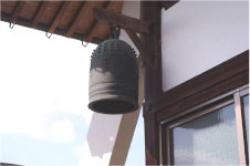 晴れた日に寺の外壁から飛び出た梁に吊るされた半鐘を少し離れた位置から撮った写真