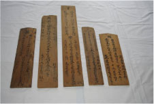 細かい字が刻まれた細長い茶色の木の板が五枚横に並べられている写真