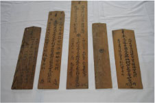 細かい字が刻まれた細長い茶色の木の板が五枚横に並べられている写真