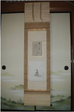 座っている女性の絵と和歌が描かれた茶色の掛け軸が襖の壁に掛けられている写真