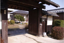 木製の柱と壁で作られ、瓦屋根が特徴的な冠木門を左前から撮影した写真
