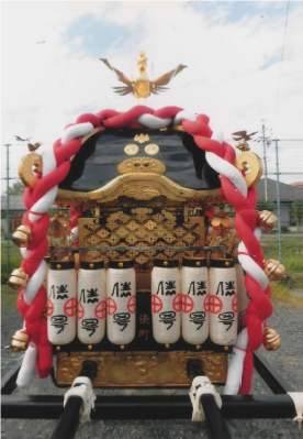 紅白のしめ縄と白いちょうちんが神輿を囲むように並べられて設置されている神輿の写真
