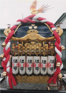 紅白のしめ縄と白いちょうちんが並んで設置されている神輿を左側面から撮影した写真