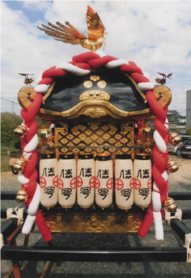 紅白のしめ縄と白いちょうちんが並んで設置されている神輿を右側面から撮影した写真