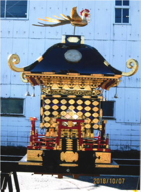 左側面から撮影した黒色と赤色が基調の頂部に鳳凰の飾りが乗った神輿の写真