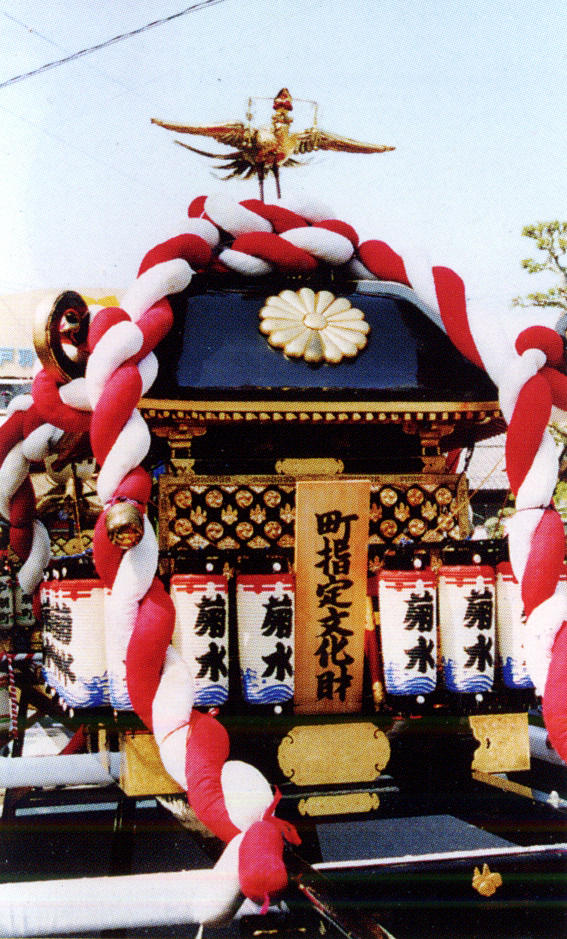 神輿の上に金色の鶏、「町指定文化財」と書かれた札があり、大きな紅白のねじり帯が神輿全体に纏うように設置されている石町の神輿の写真